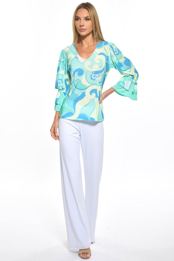 A woman wearing a blue swirl Bardot top with a V-neckline and three-quarter sleeves paired with white trousers.